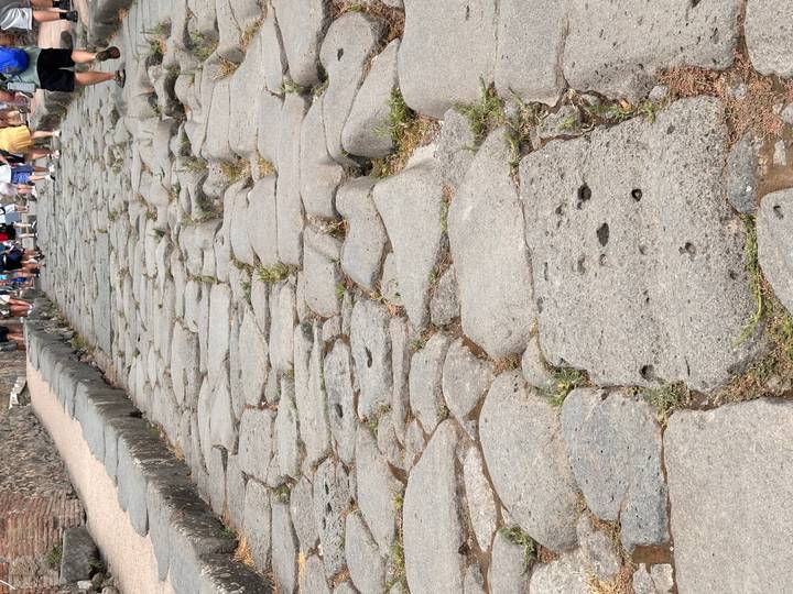 Original stone roadway in Pompeii shows deep cart ruts with tourists walking ahead.
