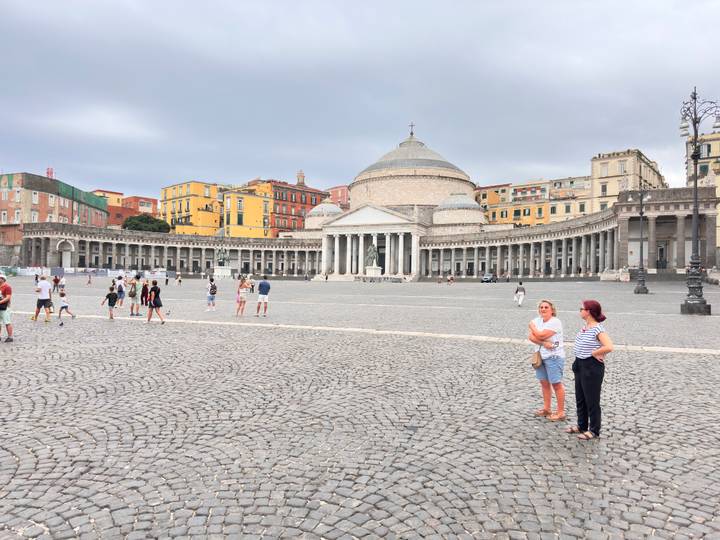 Wide cobbled Piazza del Plebiscito in Naples framed by San Francesco di Paola basilica and colorful palazzi.