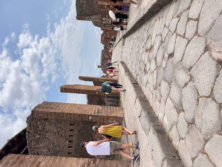 Tourists walk along a restored stone street lined with brick columns in Pompeii.