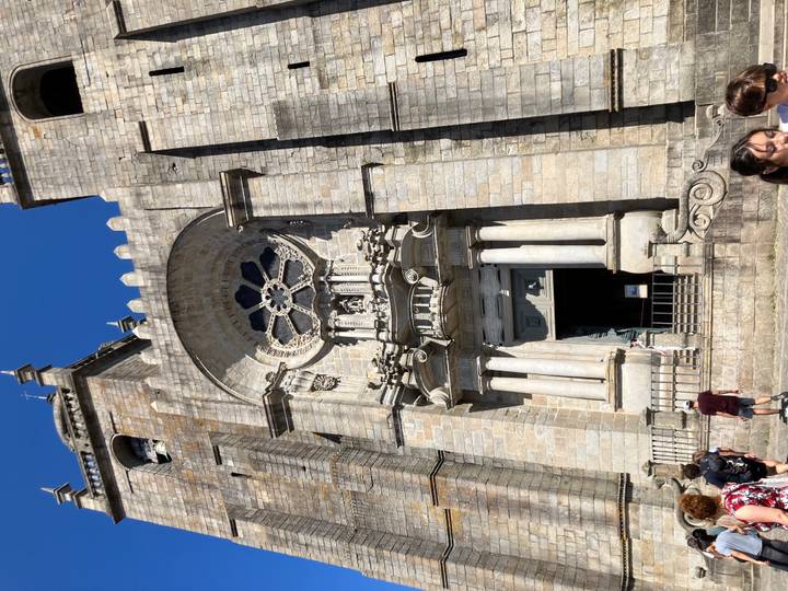Stone façade of a historic cathedral with visitors entering through an ornate doorway on a sunny day.