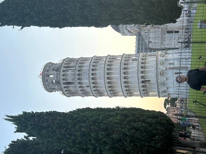 Traveller posing in front of the Leaning Tower of Pisa at dusk with soft golden light in the sky.