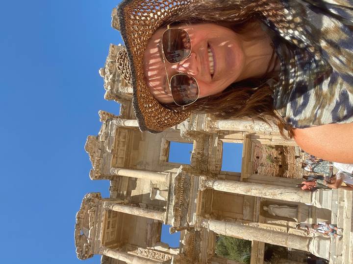 Smiling traveler taking a selfie in front of the ancient Library of Celsus ruins under clear blue sky