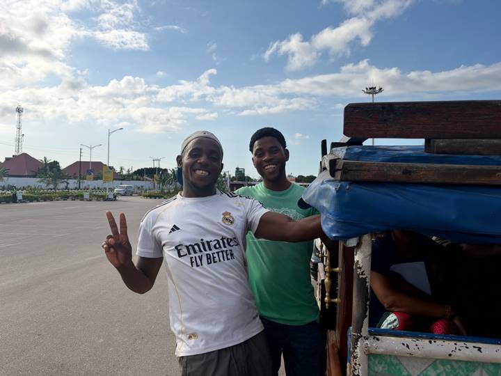 Two young men smiling beside an open truck on a sunny day in an urban lot