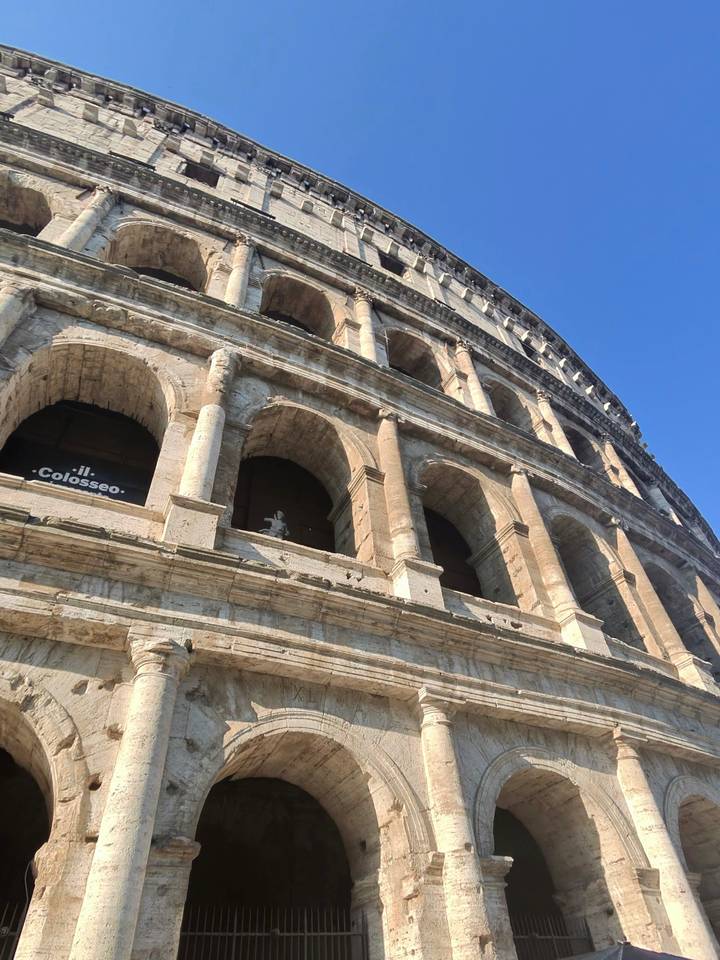 Dramatic upward angle of the stone arches of the Colosseum against a clear blue sky.