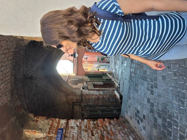 Woman in striped shirt looks down a narrow cobbled alley framed by an old brick archway.