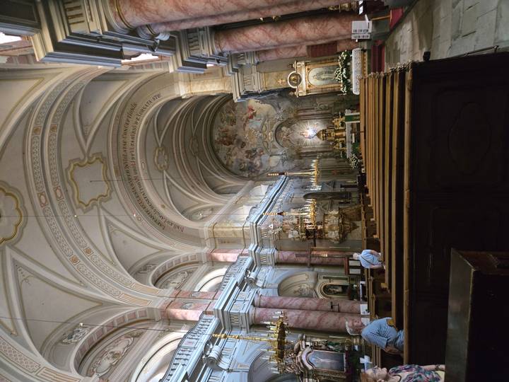 Lavish baroque church interior with pink marble columns, ornate frescoes and gilded altars illuminated by chandeliers.