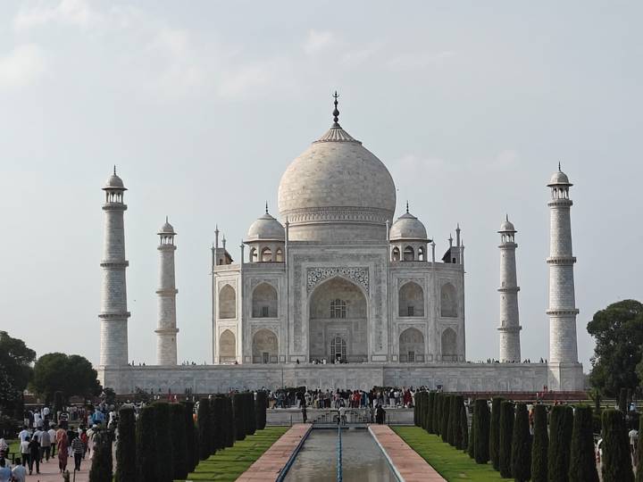 Frontal view of the Taj Mahal with its four minarets and crowds of visitors at the base under a clear sky.