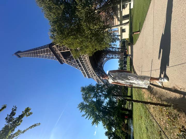 Traveler posing on a path beneath the towering Eiffel Tower on a bright blue-sky day