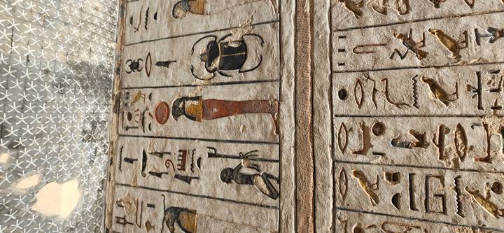 Stone wall panels covered with colorful hieroglyphs and ancient Egyptian figures under a patterned ceiling.