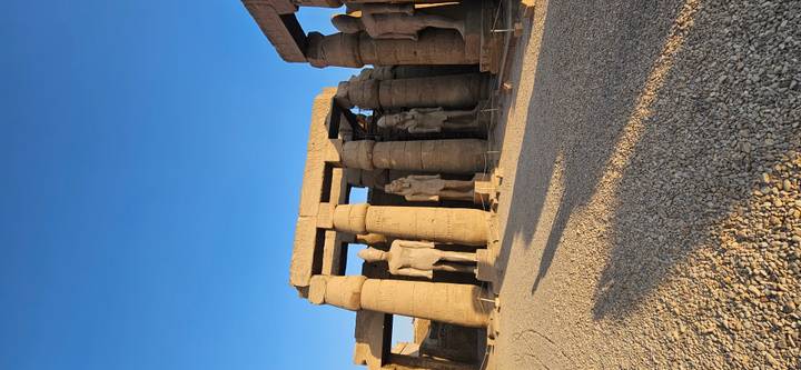 Massive stone statues and towering columns of an ancient temple glow in warm low sunlight against a clear blue sky.