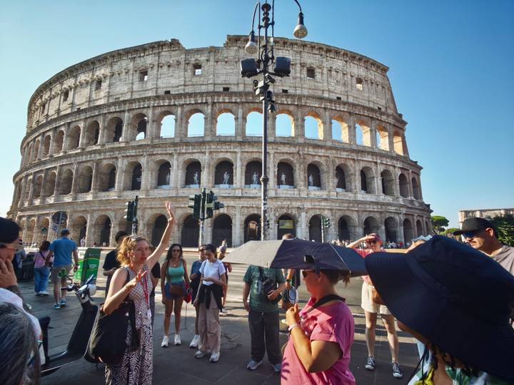 Guide raising hand while group stands before the Colosseum’s imposing facade in Rome