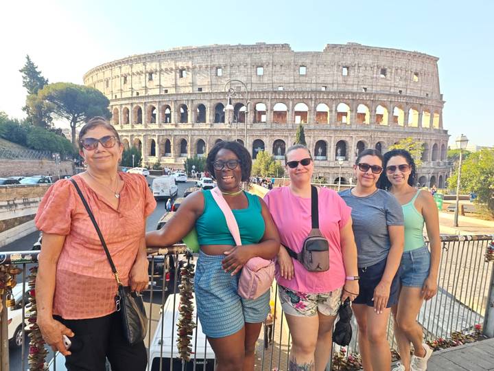 Group of women smiling on a viewpoint railing with the Colosseum in the background