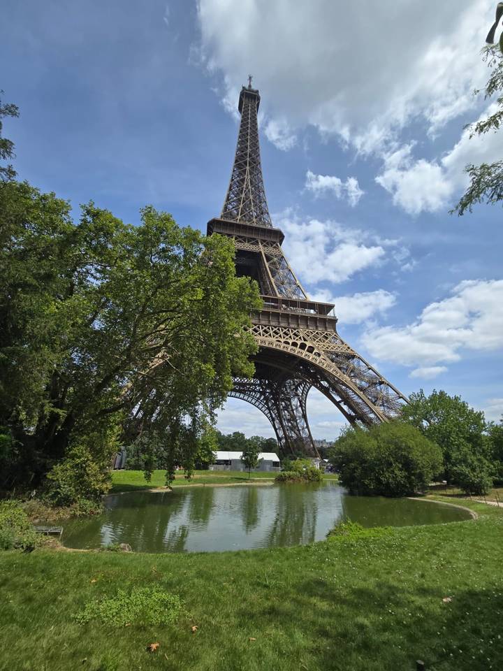 Eiffel Tower rising above leafy trees against a partly cloudy blue sky