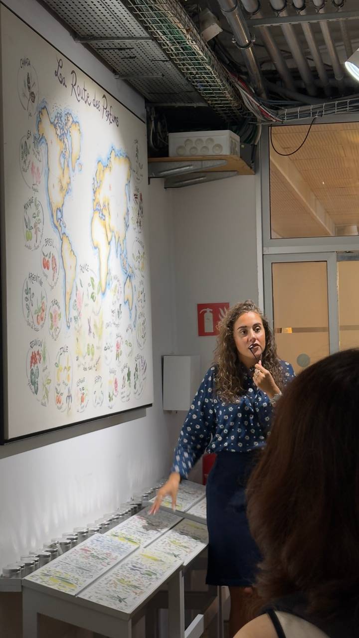 A woman gives a presentation beside an illustrated world map inside a classroom setting.
