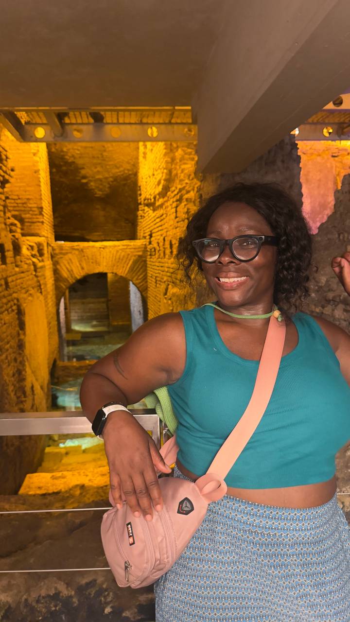Smiling visitor poses inside a dimly lit ancient brick corridor with arched passageways.