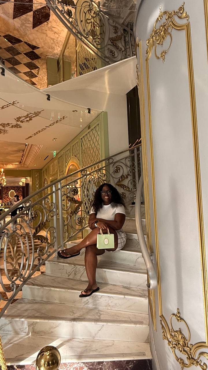Traveler sits on an ornate marble staircase inside an elegant, luxurious interior holding a shopping bag.