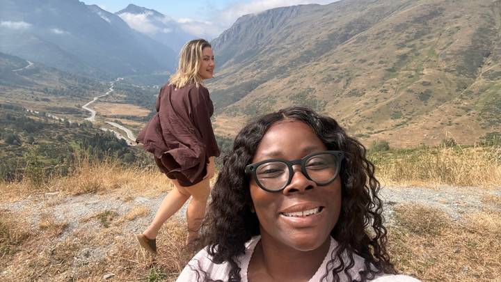 Two friends pose on a mountain overlook with valley, river and peaks stretching into the distance.