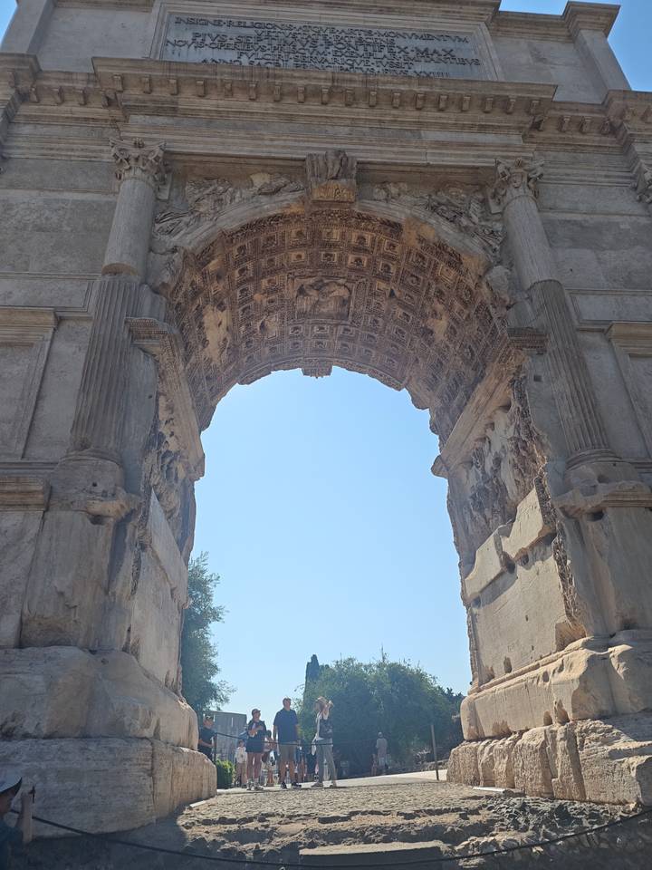 Stone archway of an ancient Roman triumphal arch rises against a clear blue sky.