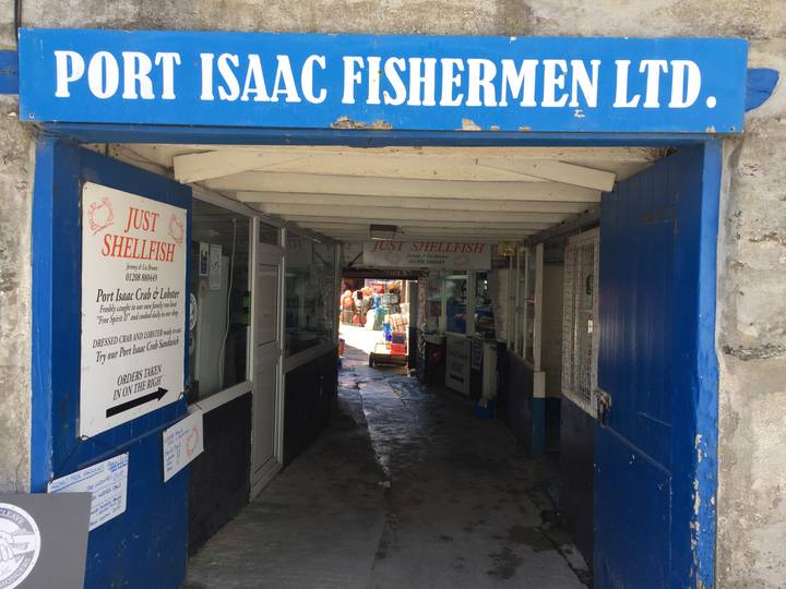 Narrow passageway to a seafood shop with blue signage reading Port Isaac Fishermen Ltd