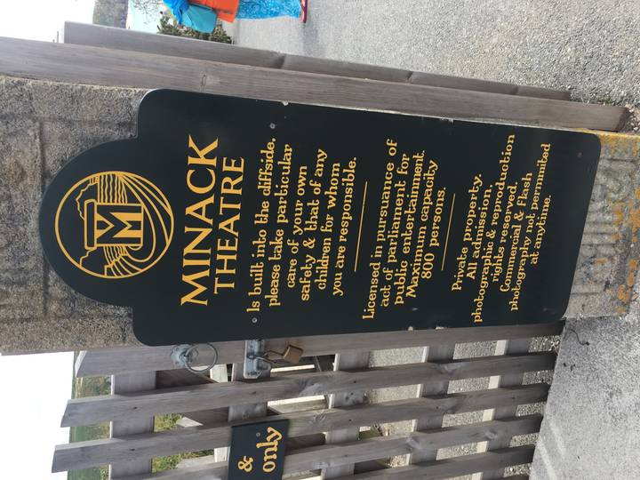 Vertical black sign describing the cliffside Minack Theatre fixed to a stone post