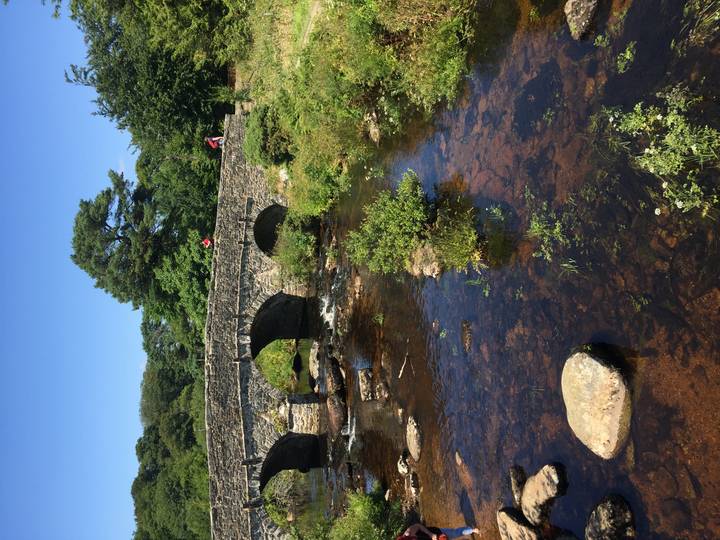 Vertical shot of stone bridge spanning a shallow river with two small human figures on top