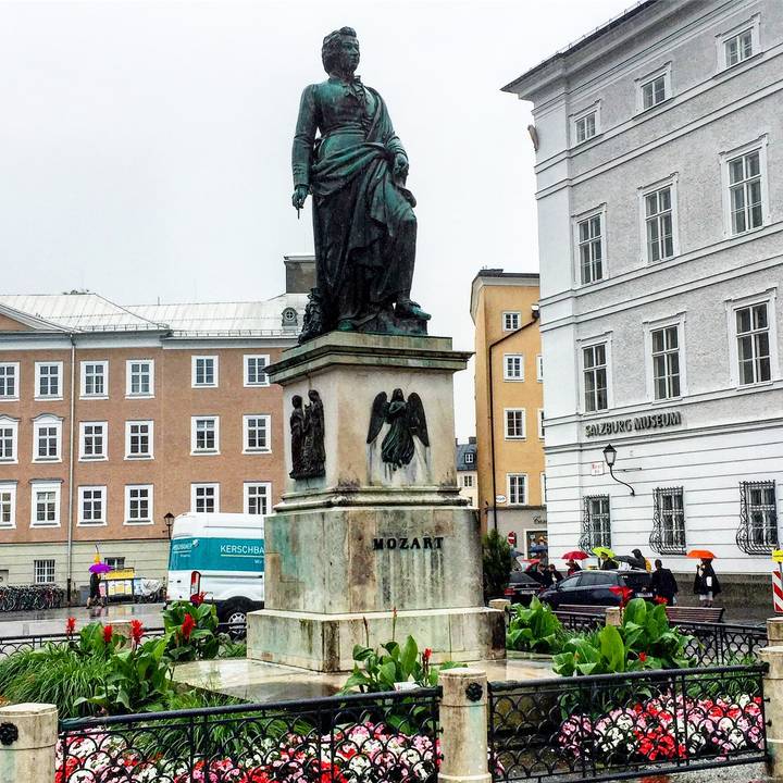 Mozart statue in Salzburg’s Mozartplatz framed by historic pastel buildings on a rainy day