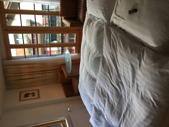 Hotel room view across rumpled white bedding toward balcony doors and a small table
