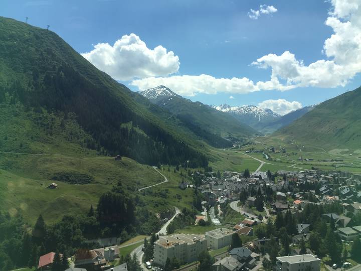 High vantage through panoramic train windows showing alpine valley town and snow-capped peaks