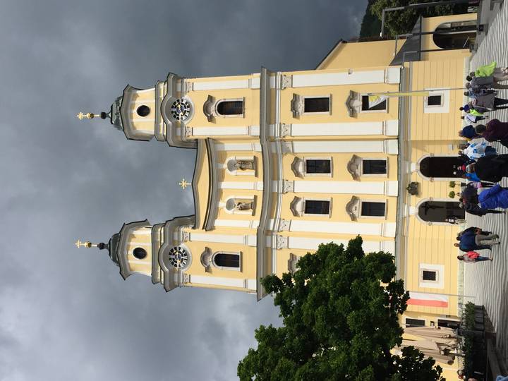 Yellow twin-tower basilica of Mondsee rising against a dramatic dark sky with tourists below