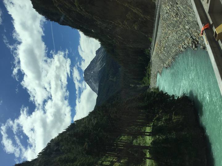 Bright turquoise alpine river winding through steep forested mountains under partly cloudy sky
