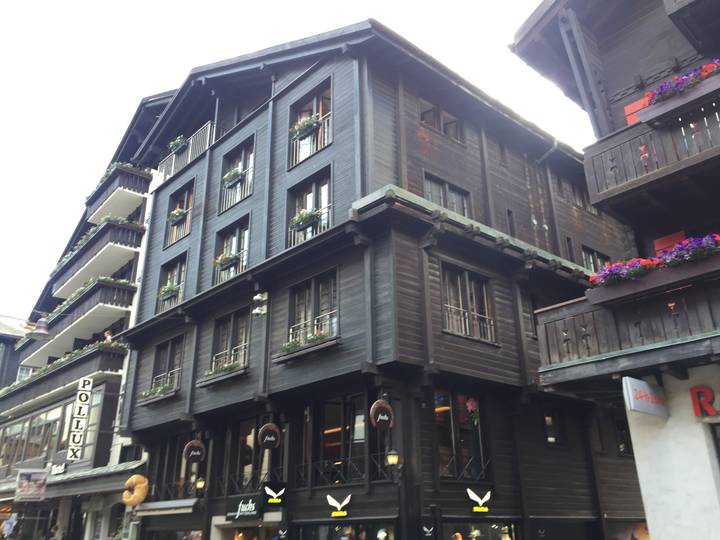 Traditional dark-wood alpine building with flower boxes and shop signs under bright sky
