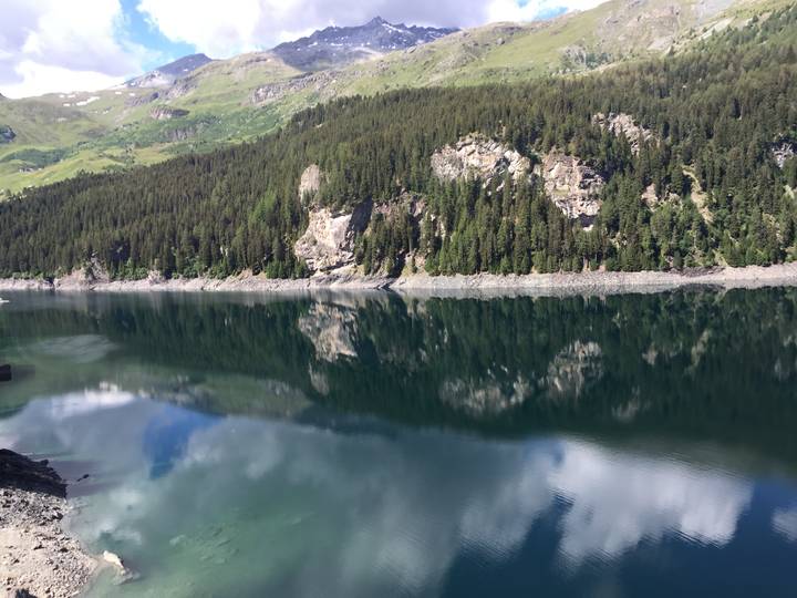 Still alpine reservoir reflecting dense pine forests and rocky slopes under clear skies