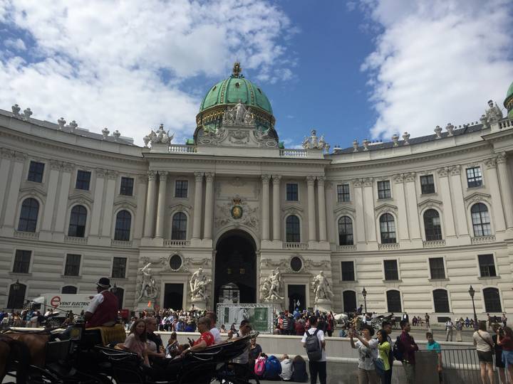 Grand Hofburg palace wing in Vienna with green dome, ornate statues and bustling visitors
