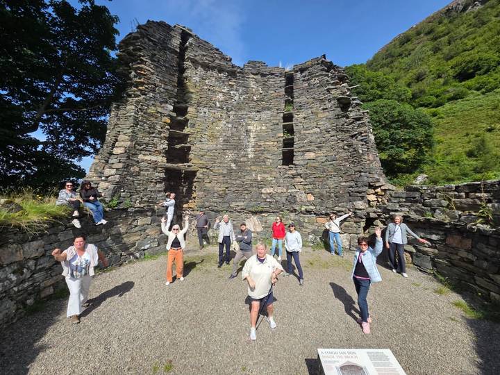 Tour group standing and waving inside the stone ruins of an ancient Scottish castle surrounded by greenery.