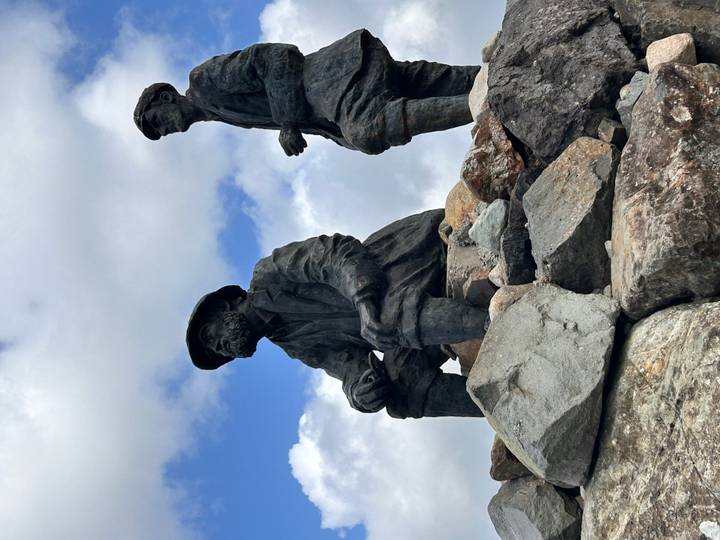 Close-up of bronze statues of two fishermen set against a partly cloudy sky.