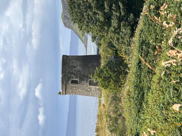 Stone tower overlooking the sea with rolling Scottish hills and cloudy skies.