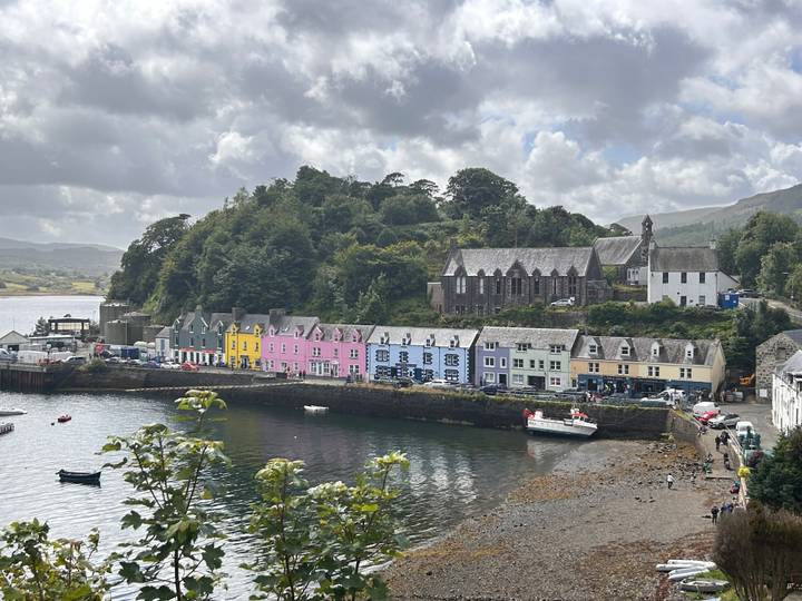 Colorful row of houses lining the harbour at Portree with boats anchored in the water under a cloudy sky.