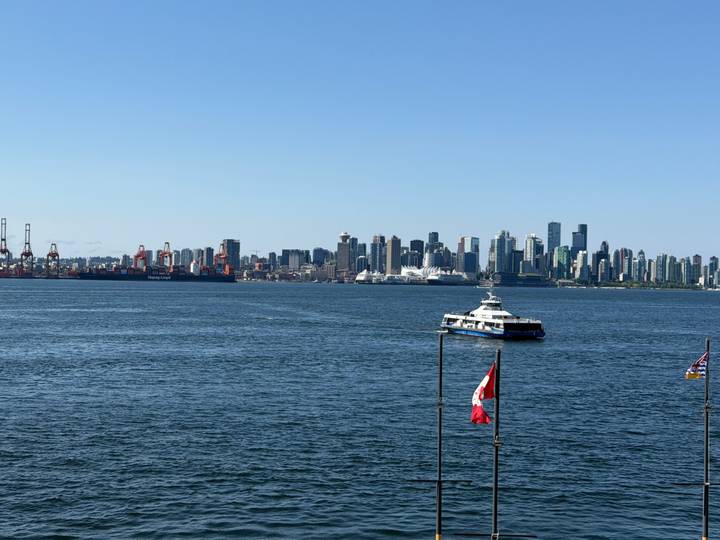 Vancouver skyline rises behind blue harbour waters with a ferry and Canadian flag in the foreground.