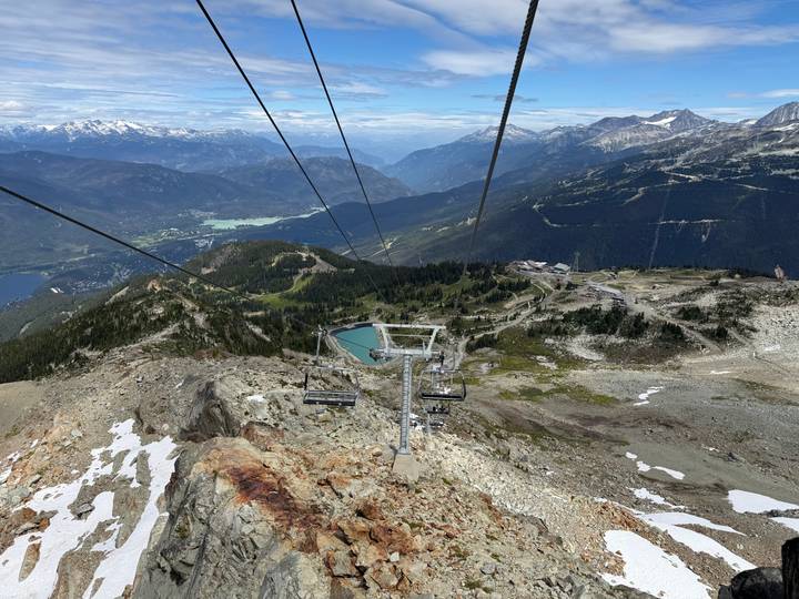Aerial view from chairlift over rugged mountain terrain, alpine lakes and distant valleys.