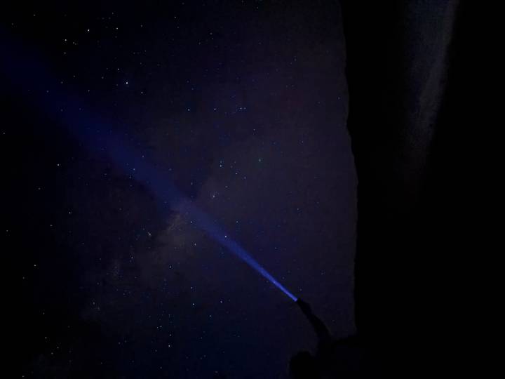 Night desert scene with a person shining a blue flashlight beam toward a star-filled sky
