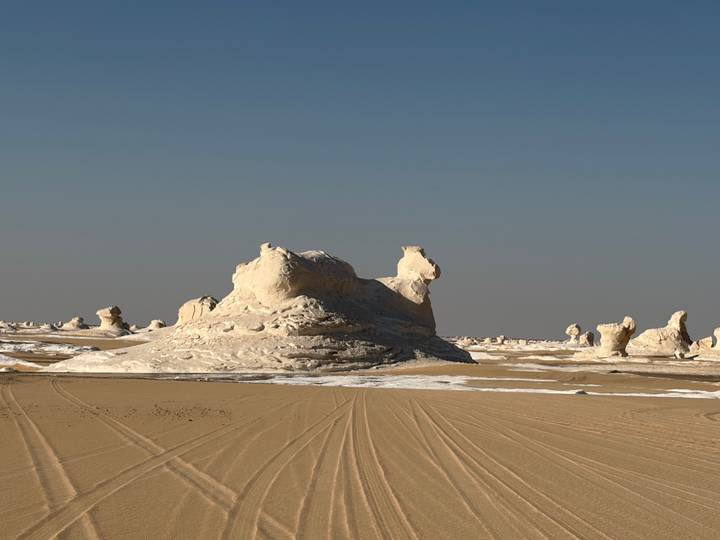 White chalky rock formations rising from the sandy desert under a clear blue sky