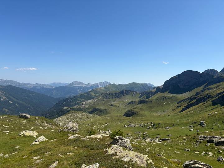 Expansive panorama of rolling green valleys and distant peaks beneath a clear alpine sky.