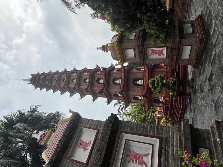 The slender brick Tran Quoc Pagoda rises between ornamental gateways against a lightly clouded sky in Hanoi.