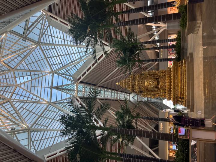 Interior of a modern airport terminal with a large golden statue beneath soaring glass and steel architecture.