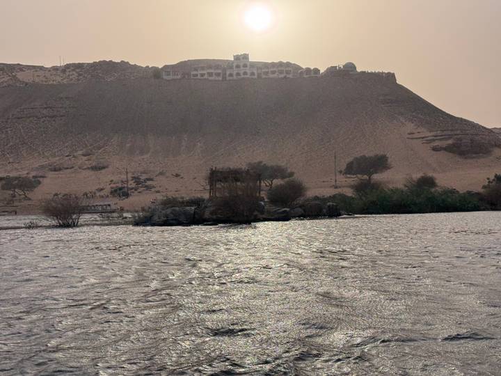 View across the Nile River toward a sandy hill crowned by a mausoleum under hazy afternoon light.