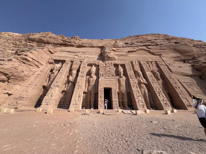 The rock-cut façade of Abu Simbel's Temple of Nefertari towers above two small visitors at the entrance.