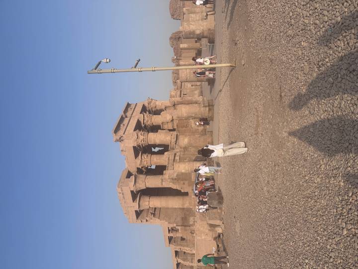 Tourists explore the sun-drenched ruins of Kom Ombo Temple under a blue sky.