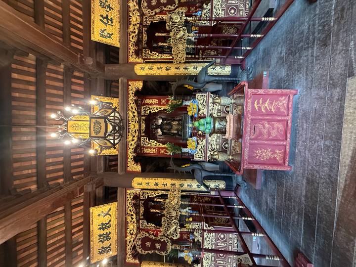 Interior of ornate Vietnamese temple with red lacquered altar and golden decorations.