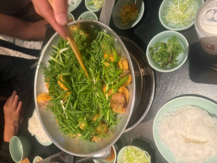 Vietnamese fish dish sizzling in a pan filled with fresh dill and herbs being stirred with chopsticks.