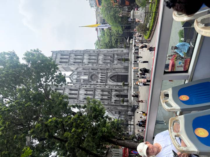 St. Joseph Cathedral in Hanoi viewed from an open-top bus with crowds outside.